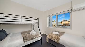 A room with two bunk beds, a window with a view of buildings, and an air conditioning unit on the wall.