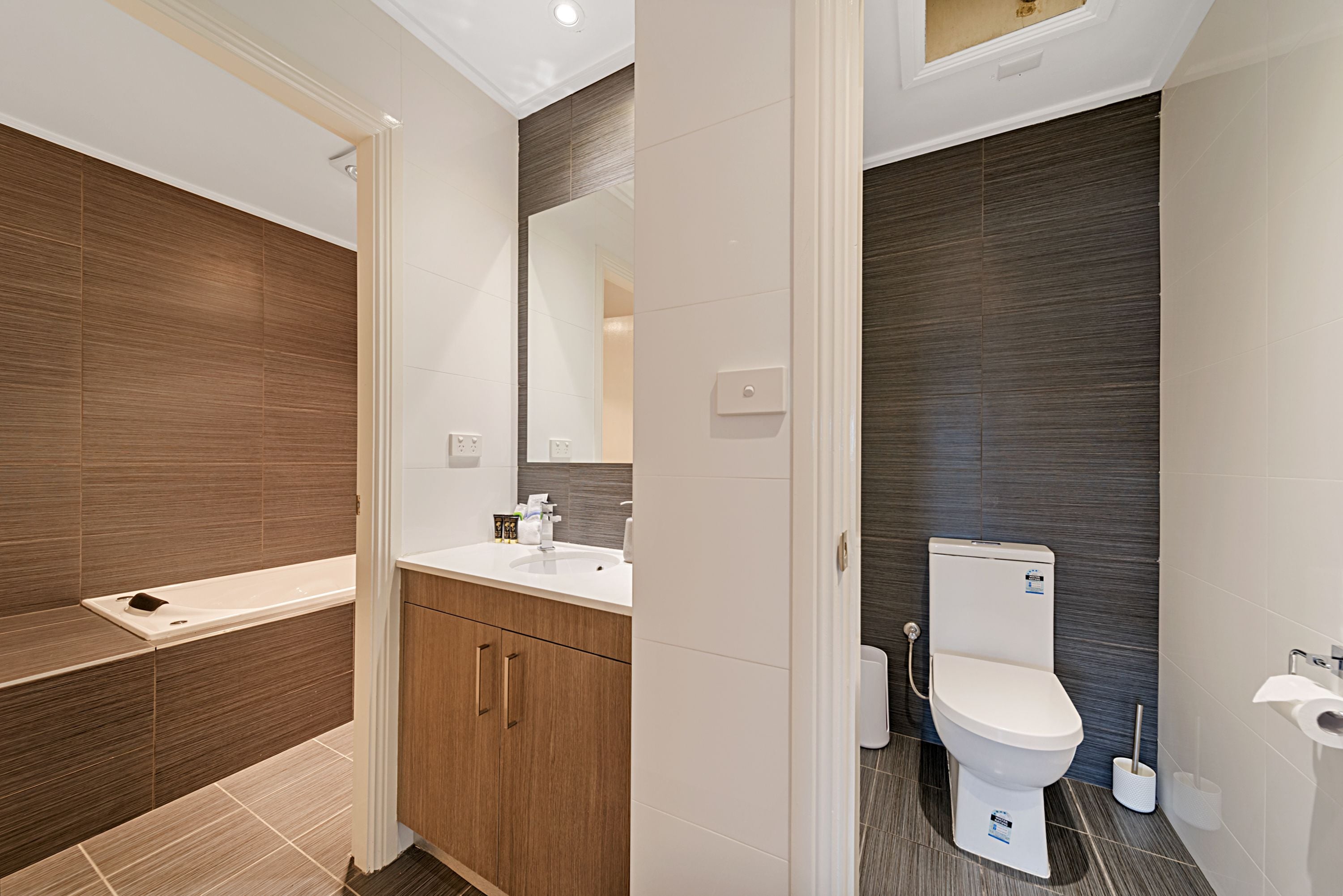 A modern bathroom with a wooden vanity, a white sink, and a toilet.