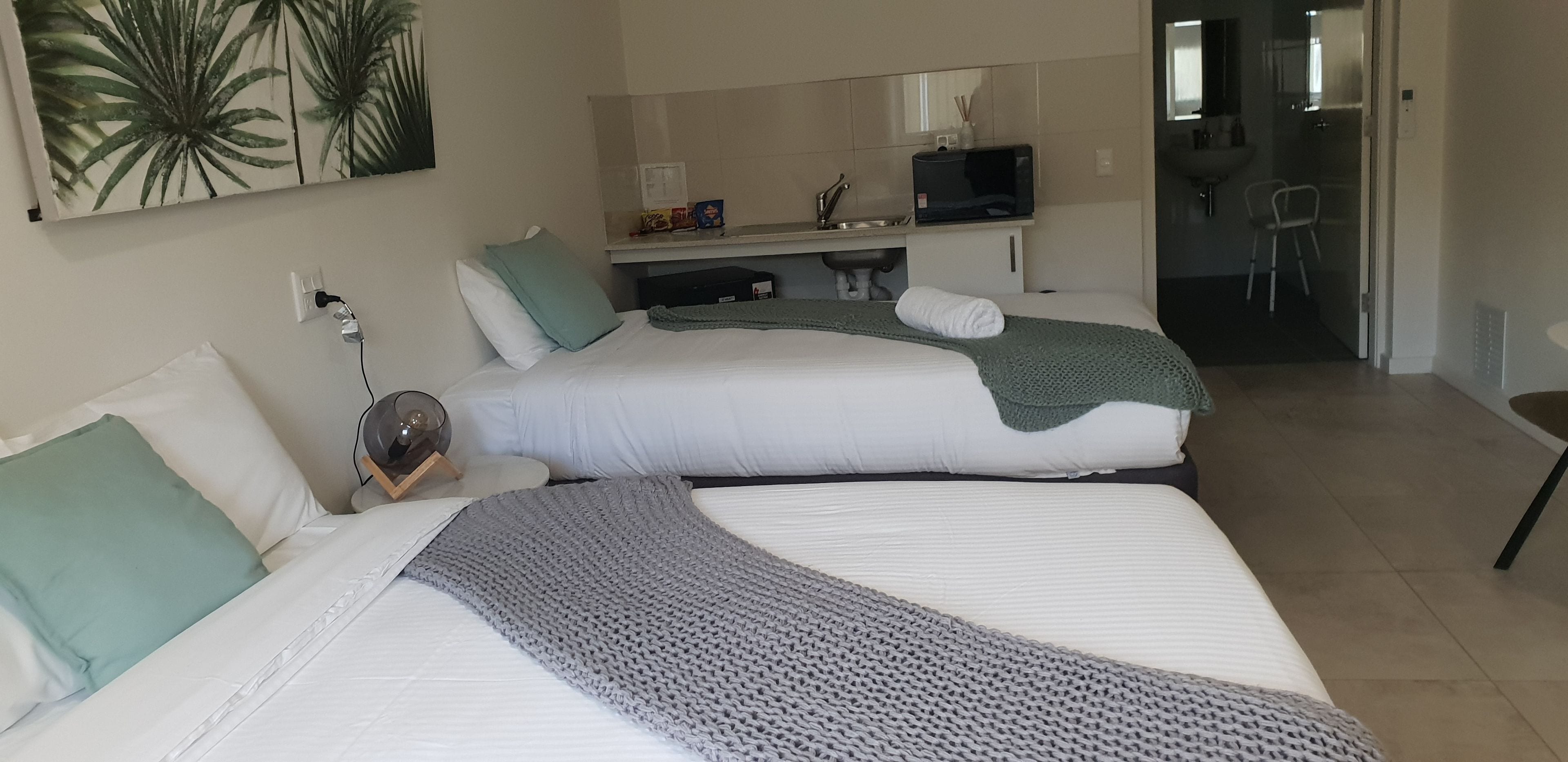 A hotel room with two beds, a flat-screen TV, a sink, and a chair.
