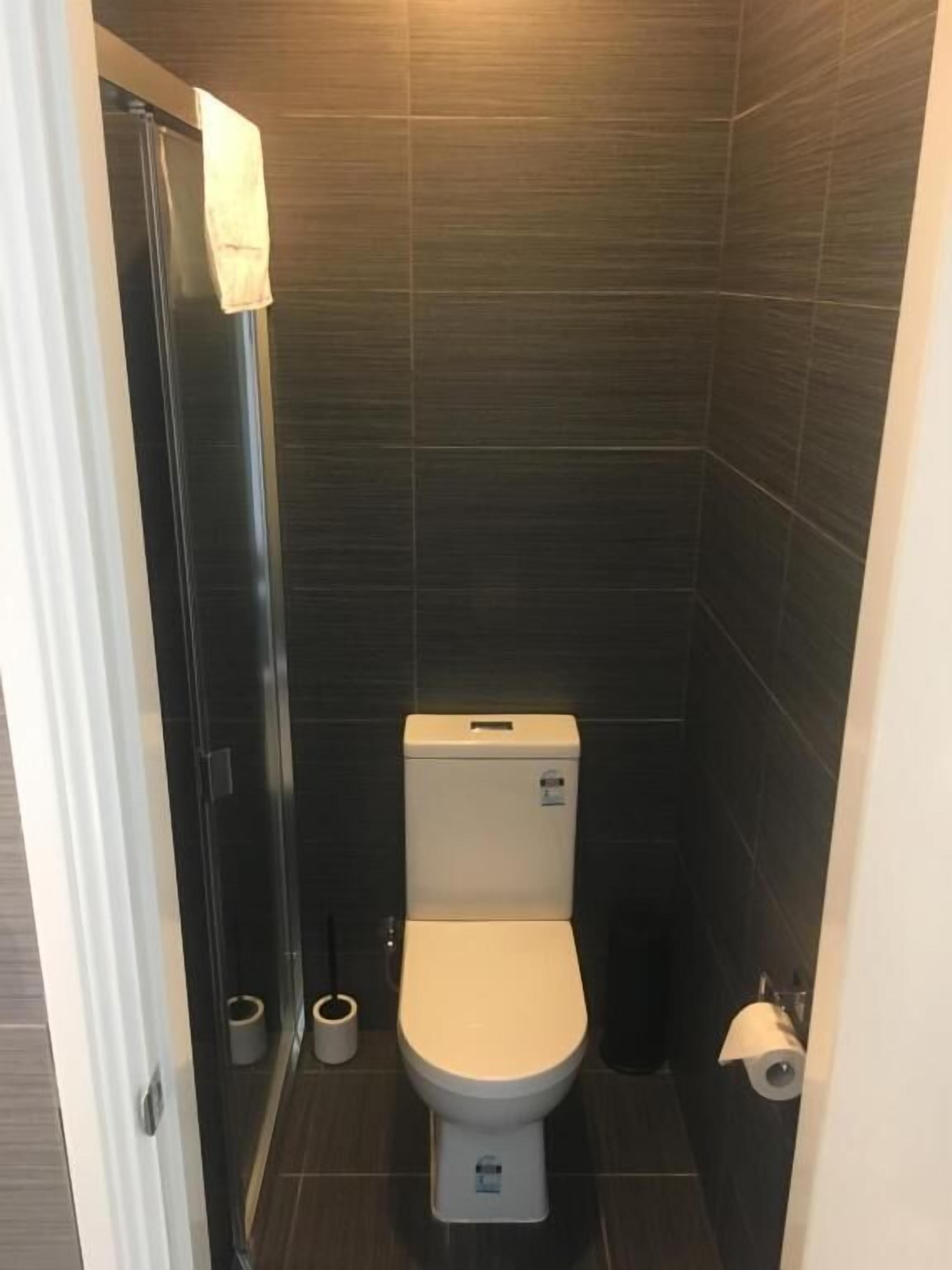 Une petite salle de bain moderne équipée d’un WC, d’une douche et d’un porte-rouleau de papier toilette.