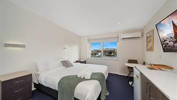 A modern hotel room with a large bed, a desk, a chair, and a window with a city view.