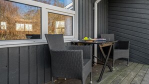 A small outdoor seating area with two wicker chairs and a table, a window with a view of trees, and a dark wooden wall.