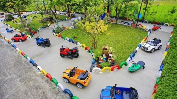Zona infantil con una pista para coches y motocicletas de juguete, rodeada de barreras de neumáticos de colores.