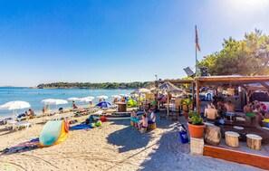 A beach with sun loungers, umbrellas, and a wooden structure with tables and chairs.