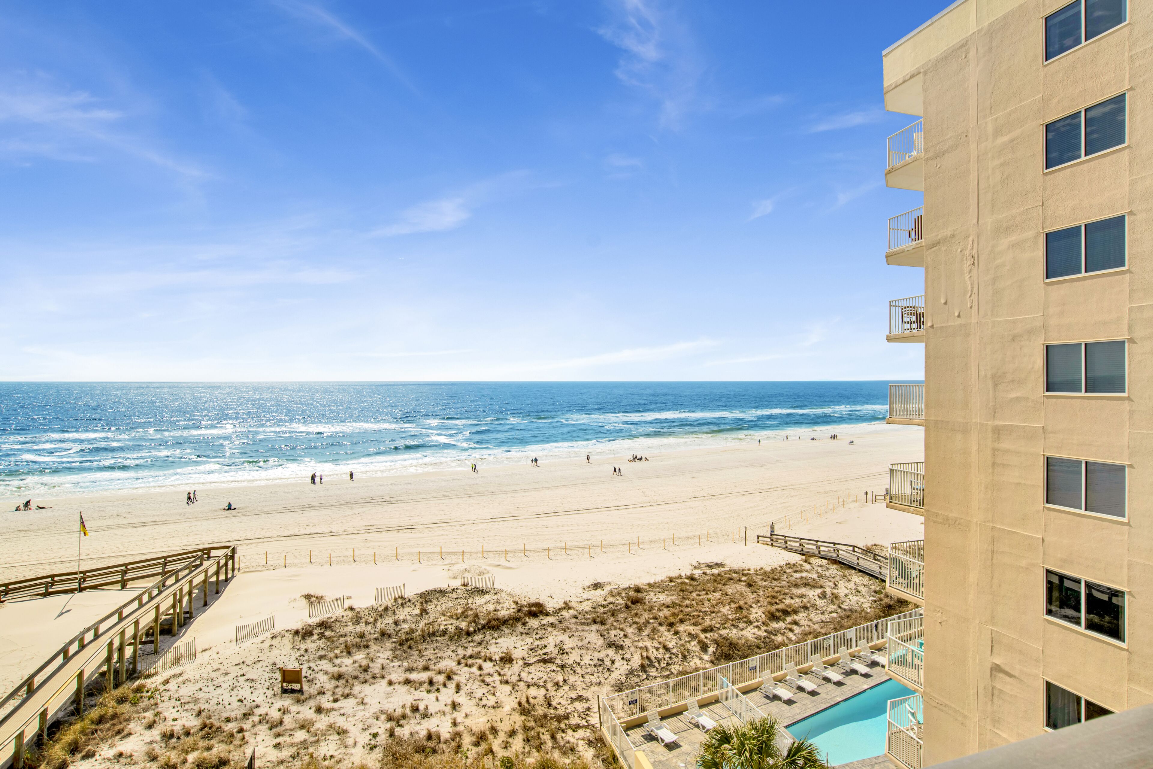 A beach view from a building with a pool and a sandy area with a wooden deck.