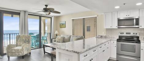 A modern kitchen with a large island, white cabinets, stainless steel appliances, and a view of the ocean through the sliding glass doors.