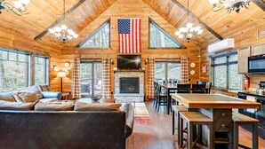 L’intérieur d’une cabane en rondins, avec une cheminée, un coin repas et un grand drapeau américain.