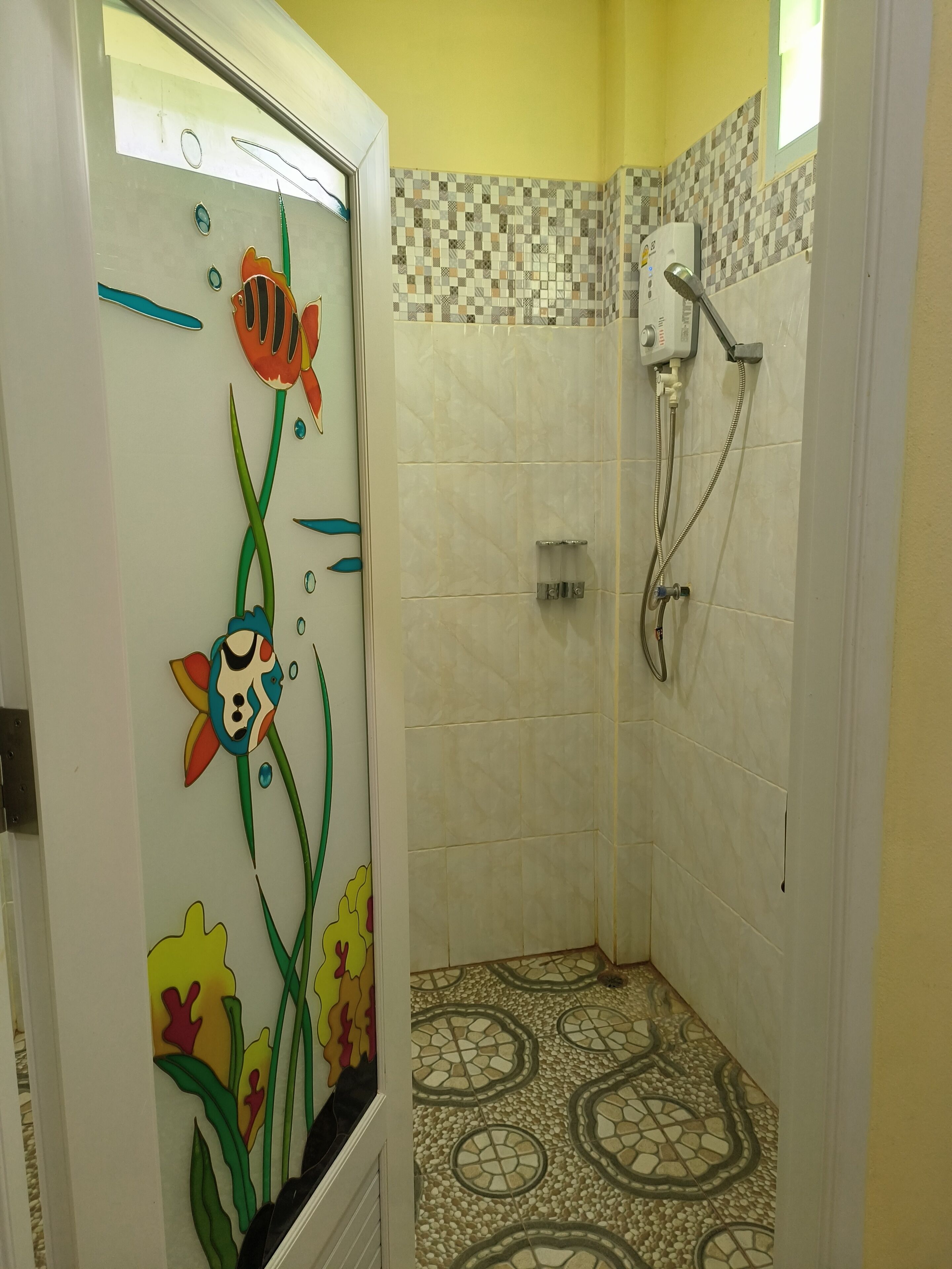 Bagno con doccia, pareti piastrellate e porta in vetro decorata con motivi floreali e pesci.