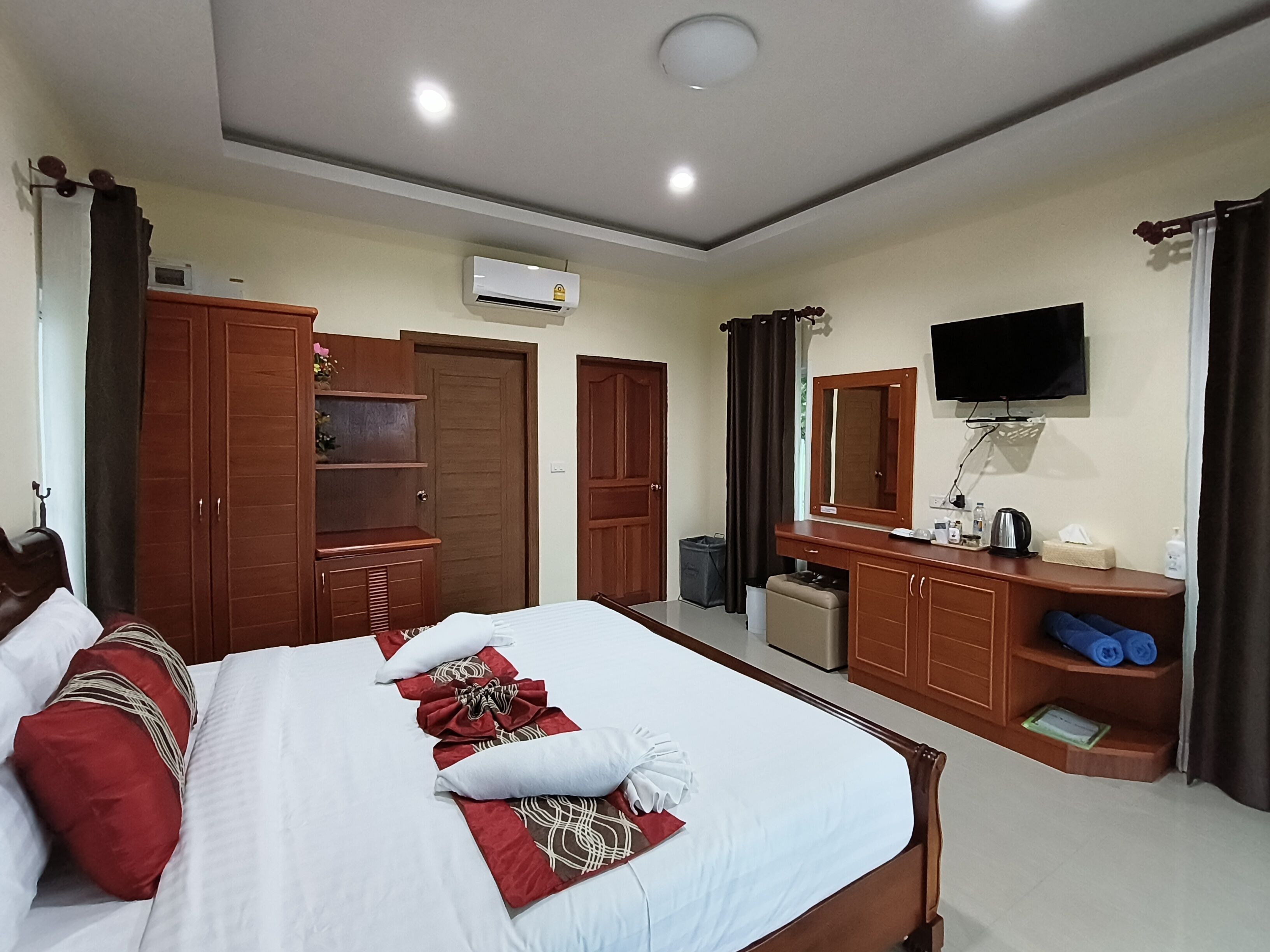 A hotel room with a bed, wardrobe, mirror, television, and a small desk with toiletries.