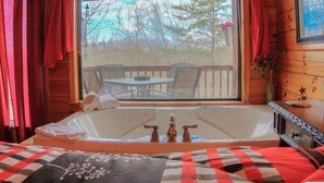 Ein Zimmer in einer Holzhütte mit einem großen Fenster, einer Badewanne und einem Esstisch vor der Tür.