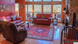 Ein geräumiges Wohnzimmer mit hoher Decke, großen Fenstern, einem roten Sofa, einem Holztisch und einem roten Sessel.