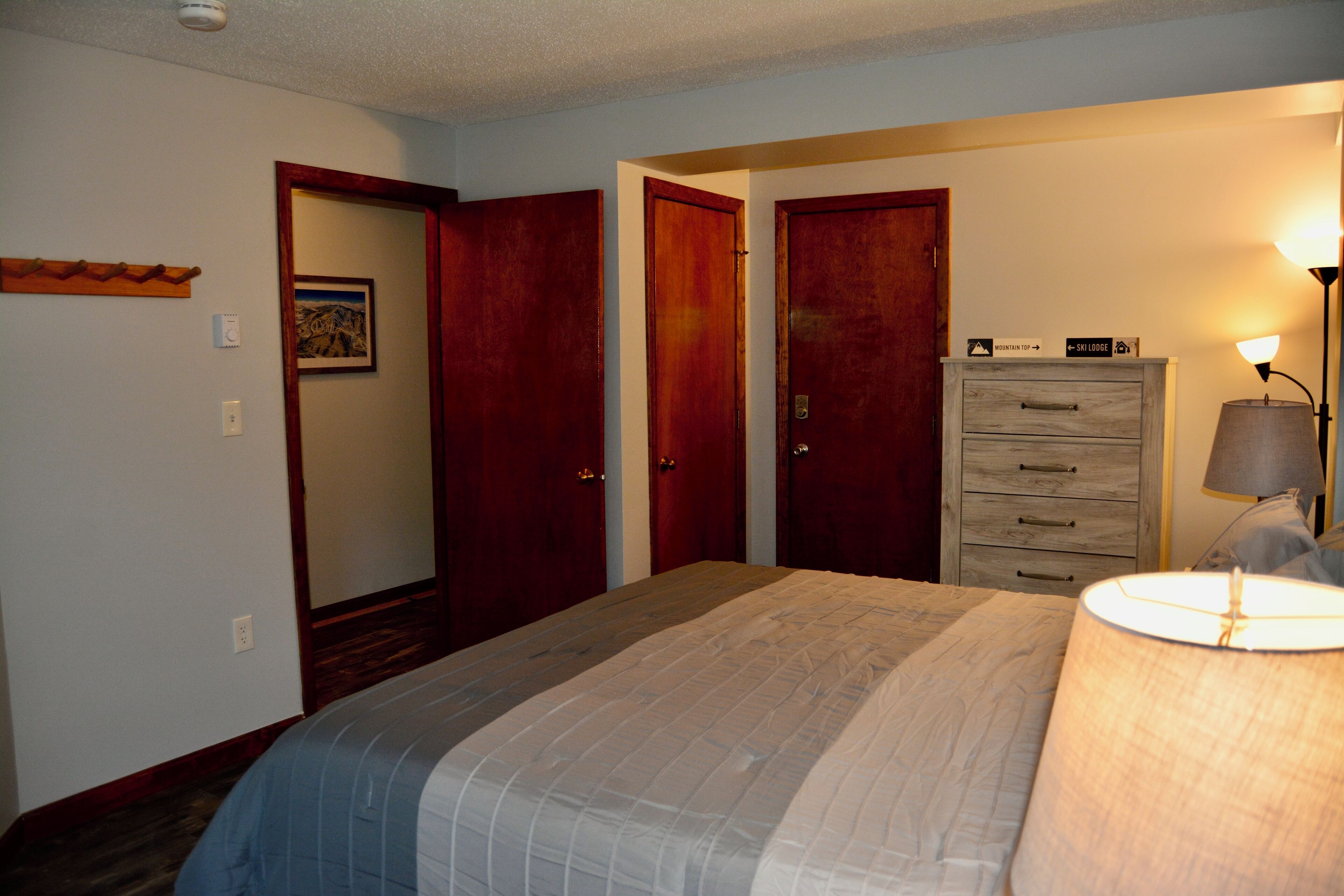 A bedroom with a bed, two doors, a dresser, and a lamp.