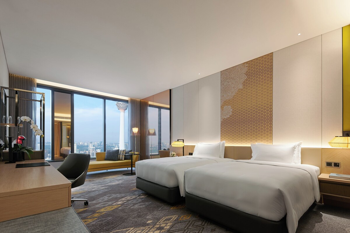 A modern hotel room with a large bed, a desk, a chair, and a view of the city skyline.