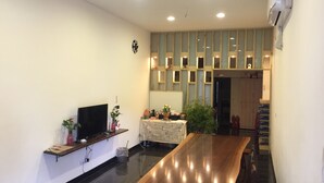 A modern living room with a wooden dining table, a flat-screen TV, and a decorative wall with recessed lighting. - Guxiang Homestay (Fuli)
