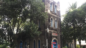 A historic building with arched windows and a blue door, surrounded by lush greenery. - Guxiang Homestay (Fuli)