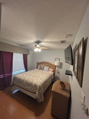 A bedroom with a bed, a ceiling fan, a window with curtains, a bedside table, and a wall-mounted TV. - Foley. 20 mins to beaches, close to Tanger Outlet, Owa, sports complex (Foley)