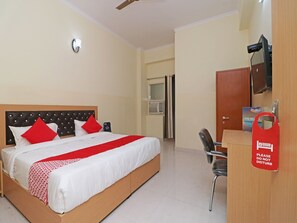 A hotel room with a bed, a desk, a chair, a TV, and a door. - OYO 28629 Crosswind Gold (Noida)