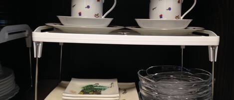 A white tray holding two white cups with colorful patterns and saucers, stacked on a white shelf. Below, there are folded white napkins and a clear plastic container.