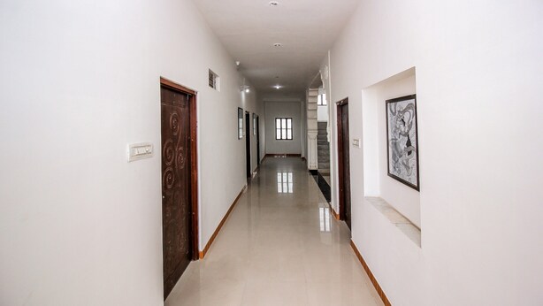 A long, narrow hallway with white walls and a tiled floor. There are doors on both sides, and a staircase is visible in the distance. - OYO 18272 Hotel Lambodar (Pushkar)