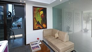 A modern living room with a beige sofa, a coffee table with magazines, and a painting on the wall. - OYO 28616 Hotel New View (Gurugram)