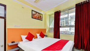 A hotel room with a bed, red curtains, a window, and a painting on the wall. - OYO 28054 Hotel Suraj Villa (Jaipur)