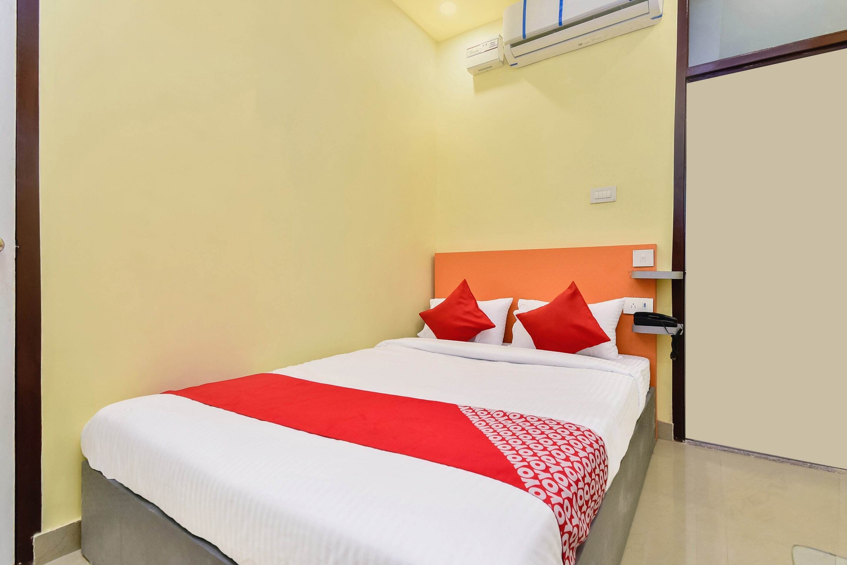 A hotel room with a bed, a red and white bedspread, and an orange headboard.