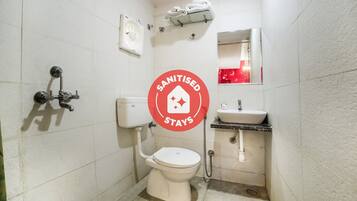 A small, white bathroom with a toilet, sink, and shower. There is a sign indicating the bathroom is sanitized.