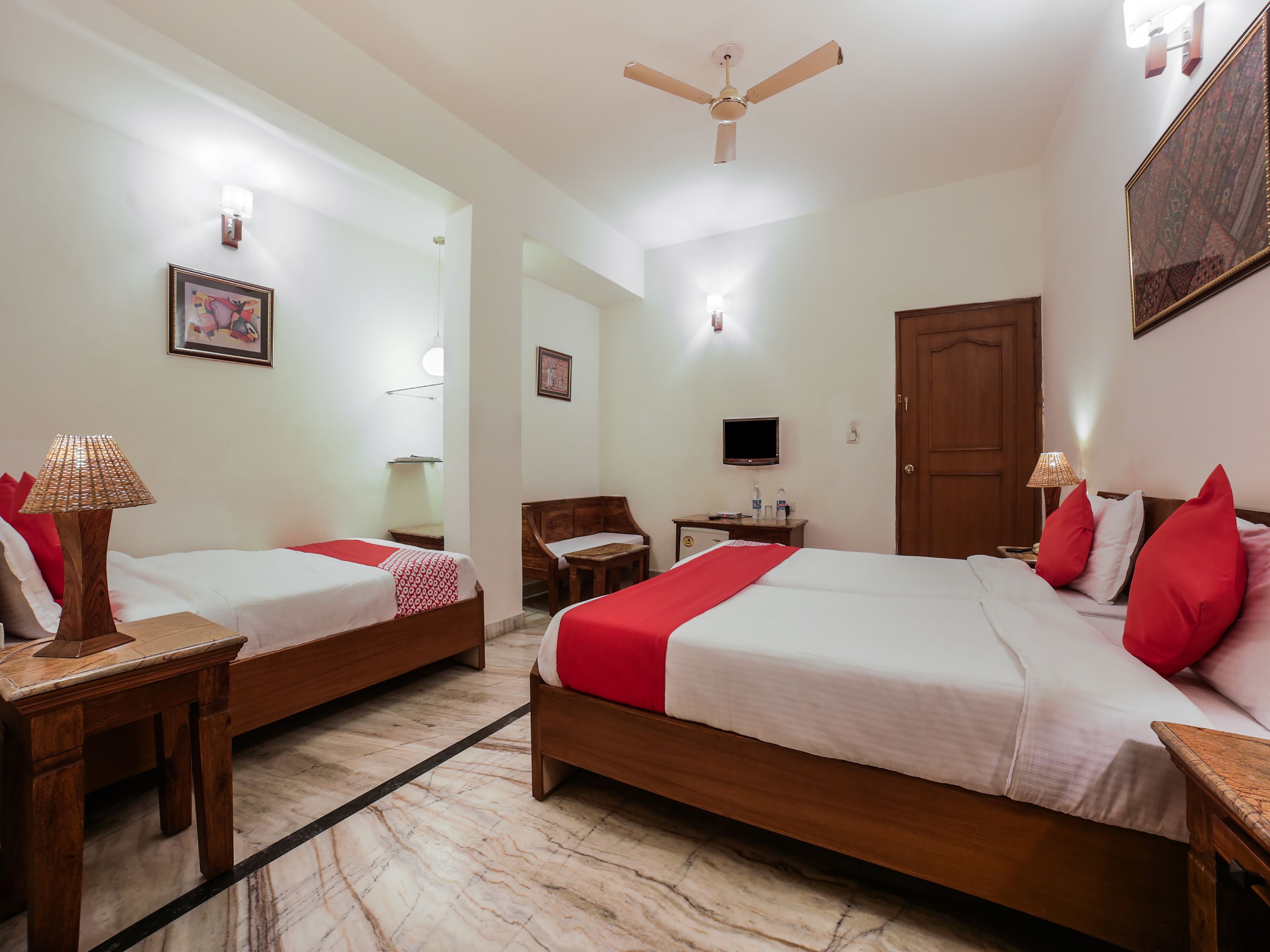 A hotel room with two beds, a desk, a chair, a television, and a ceiling fan.
