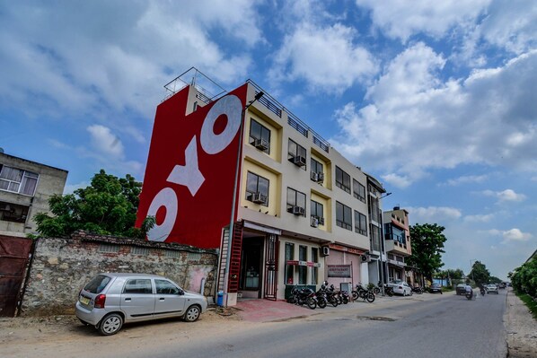 A building with a large red sign, a parked car, and a motorcycle. - OYO 17250 Hotel Ganesham (Jaipur)