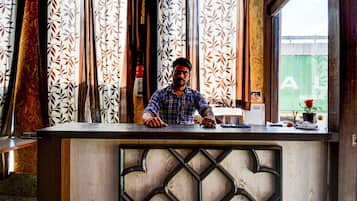 A man standing behind a reception desk with patterned curtains and a wooden design.