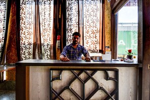 A man standing behind a reception desk with patterned curtains and a wooden design. - OYO 17250 Hotel Ganesham (Jaipur)