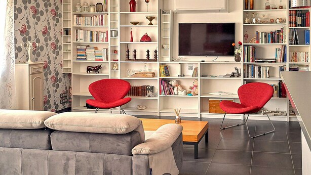 A modern living room with a grey sofa, two red chairs, a flat-screen TV, and a bookshelf filled with books and decorative items. - 2 bedroom awesome apartment in Sauvian (Sauvian)