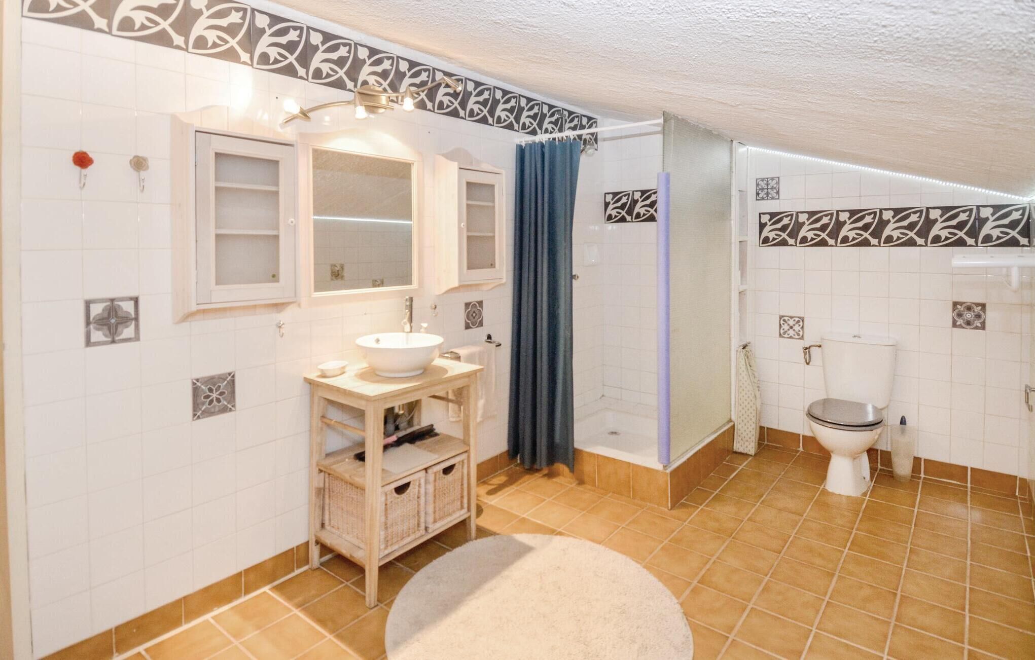 A bathroom with a white sink, mirror, and toilet, a shower curtain, and patterned tiles on the walls and floor.