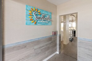 Un couloir avec un plancher en bois, un mur bleu orné d’une enseigne indiquant « Sandcastle », et un chariot visible au fond.