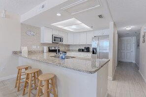 A kitchen with white cabinets, a granite countertop, a stainless steel refrigerator, and wooden stools.