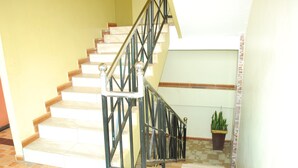 Una escalera con barandilla de metal, una planta en maceta y suelo de baldosas.