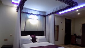 A bedroom with a bed, curtains, a bedside table, and a small desk. - Rubax Motel (Mbarara)