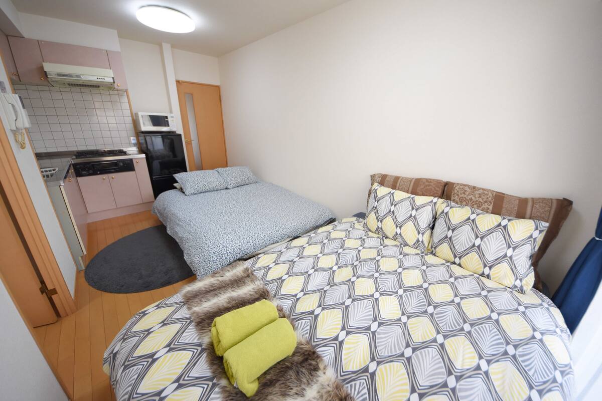 Een kleine slaapkamer met een bed, een kitchenette en een badkamer.