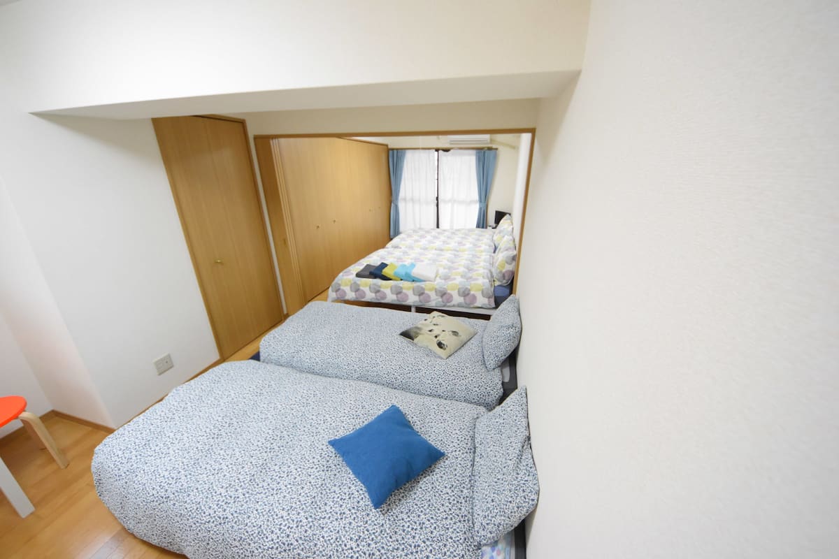 Een kleine, compacte kamer met twee bedden, een houten garderobe en een tafeltje.