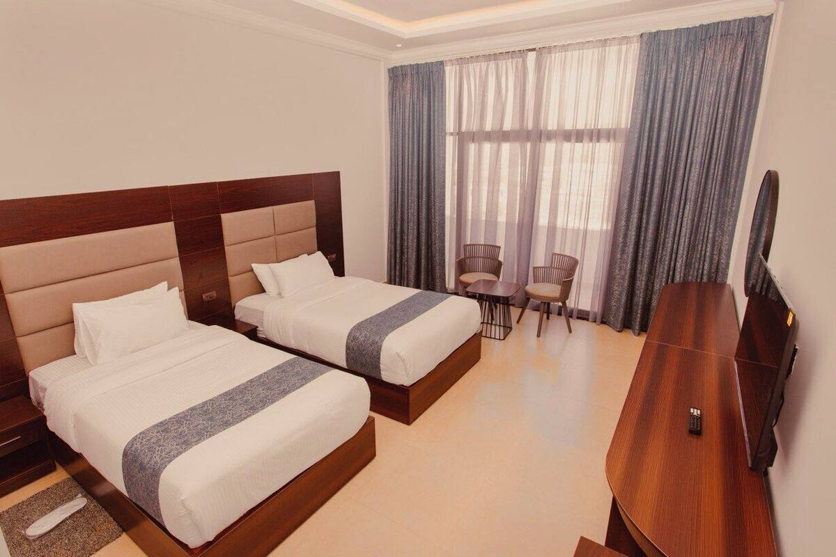 A hotel room with two beds, a desk, a chair, and a TV.