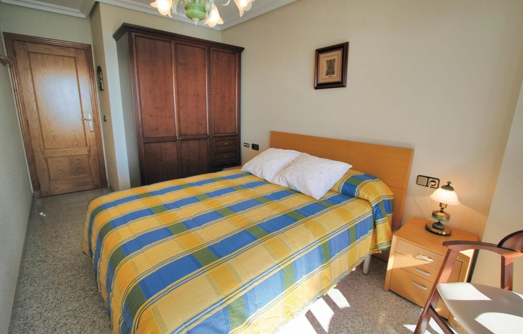 A bedroom with a bed, wooden wardrobe, and a nightstand with a lamp.