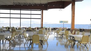 An outdoor dining area with tables and chairs, a view of the sea, and a sign for 'Newi Resort'.