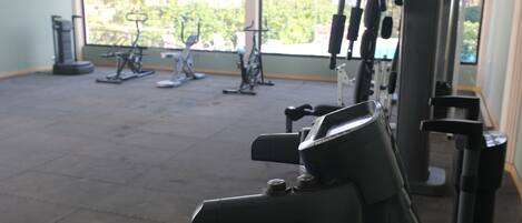 A gym with exercise equipment and a large window providing a view of greenery outside.