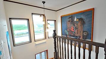 A staircase with a wooden handrail, a painting on the wall, and three windows with views of the outdoors.