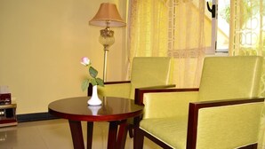 A room with a round wooden table, two yellow upholstered chairs, a white vase with a pink flower, and a floor lamp. - Lewi Hotel Piazza (Awassa)