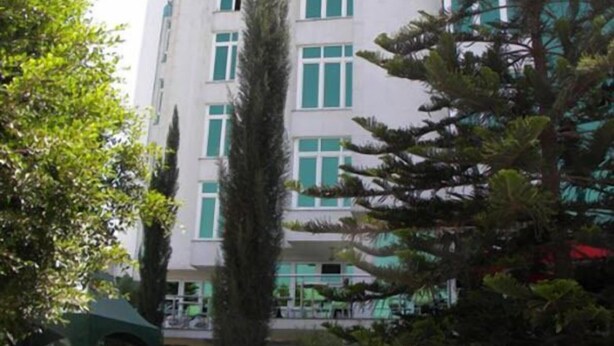 A multi-story building with a white facade and green accents, surrounded by greenery and a covered outdoor area. - Lewi Hotel Piazza (Awassa)