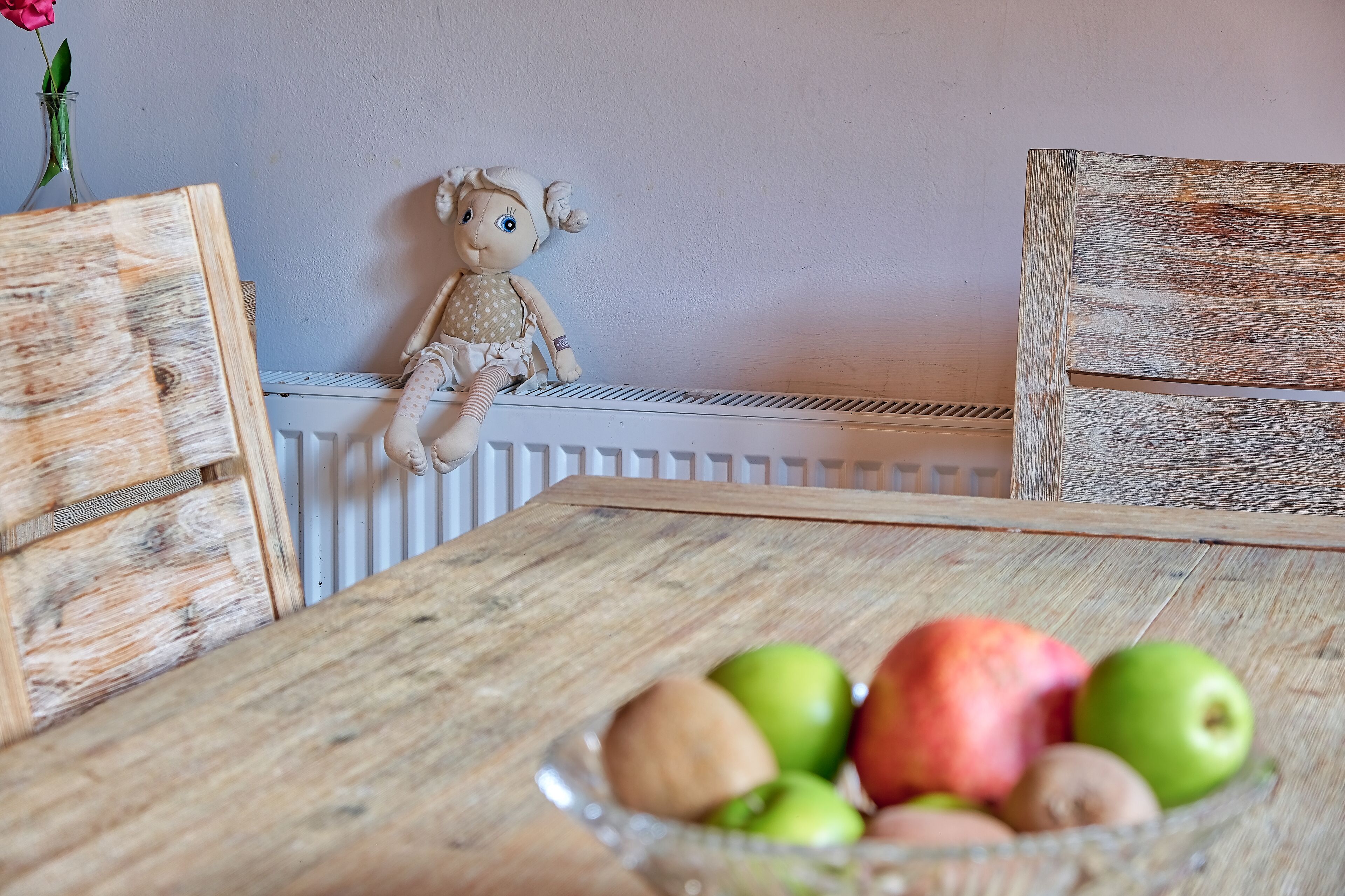 Ein Holztisch mit einer Obstschüssel und einer Puppe auf einem Stuhl.