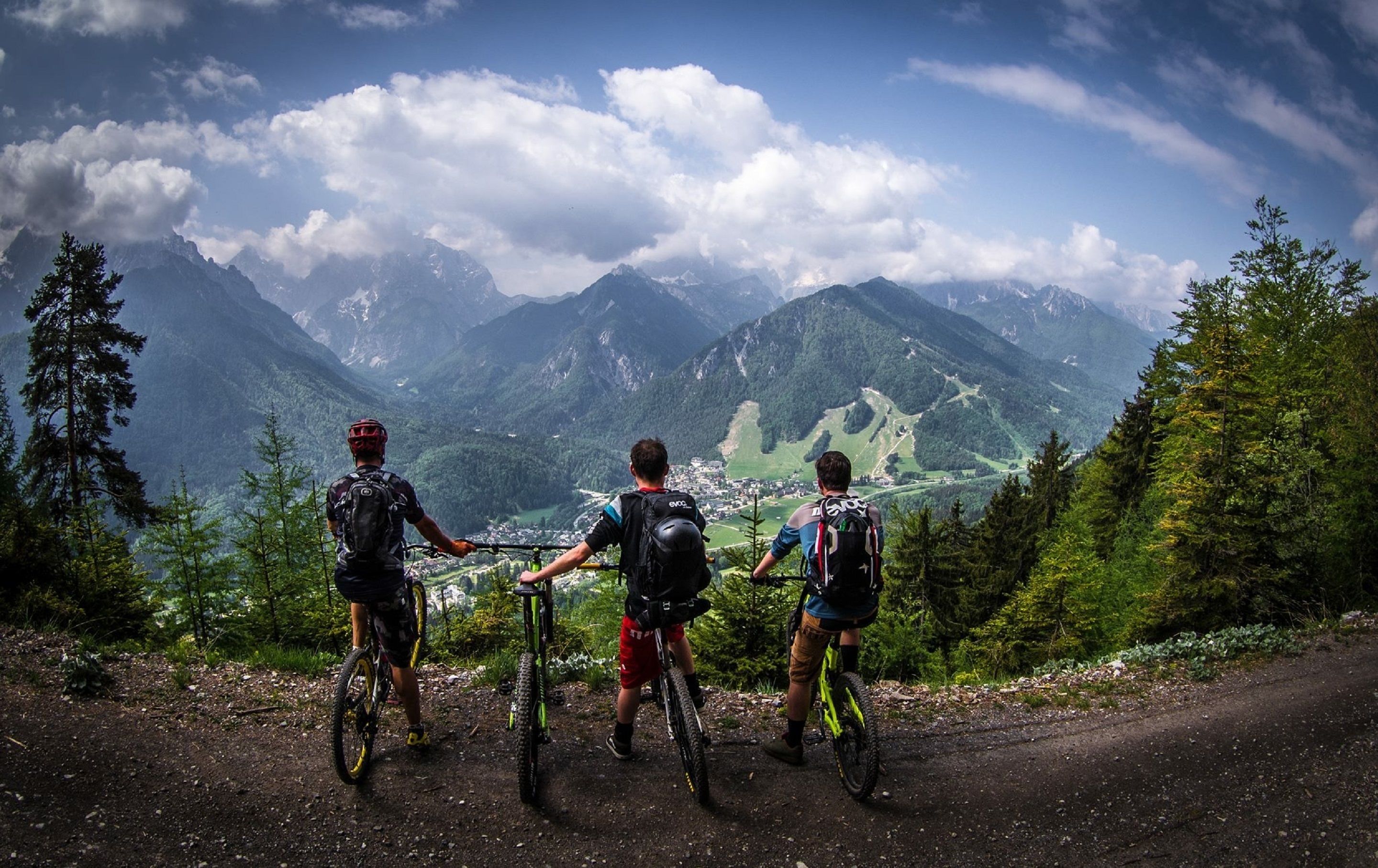Tre cyklister på en bergstig med utsikt över en dal och berg i bakgrunden.