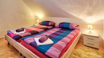 A twin bed with a colorful quilt, two pillows, a bedside lamp, and a wooden nightstand.
