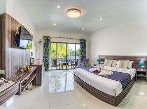 A modern hotel room with a large bed, a TV mounted on the wall, a balcony with a chair, and a fruit bowl on the side table. - The Coconut Resort (Patong)